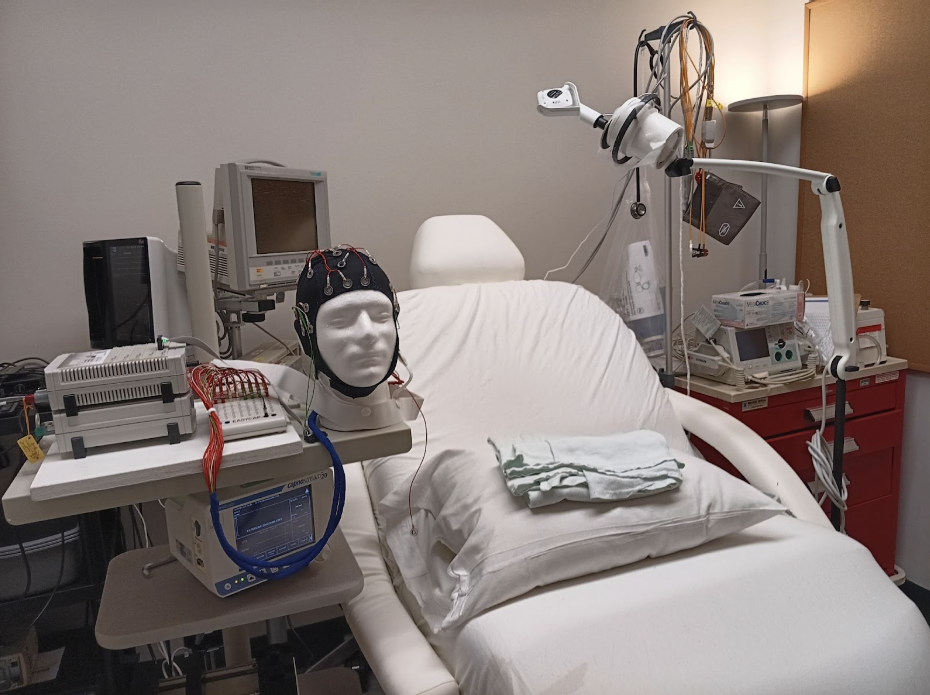 Medical room with an examination chair, EEG equipment, mannequin head with electrodes, and various medical devices.